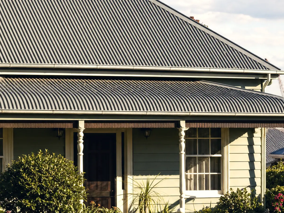 A Mayfield weatherboard cottage with a faded Colorbond roof and bullnose verandah, harbour industry far behind