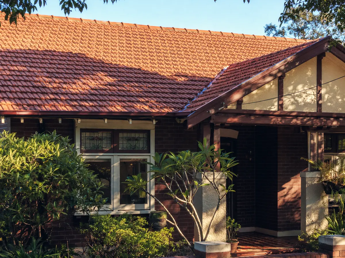 A 1920s New Lambton bungalow, broad terracotta tile gable and deep eaves under a canopy of mature street trees