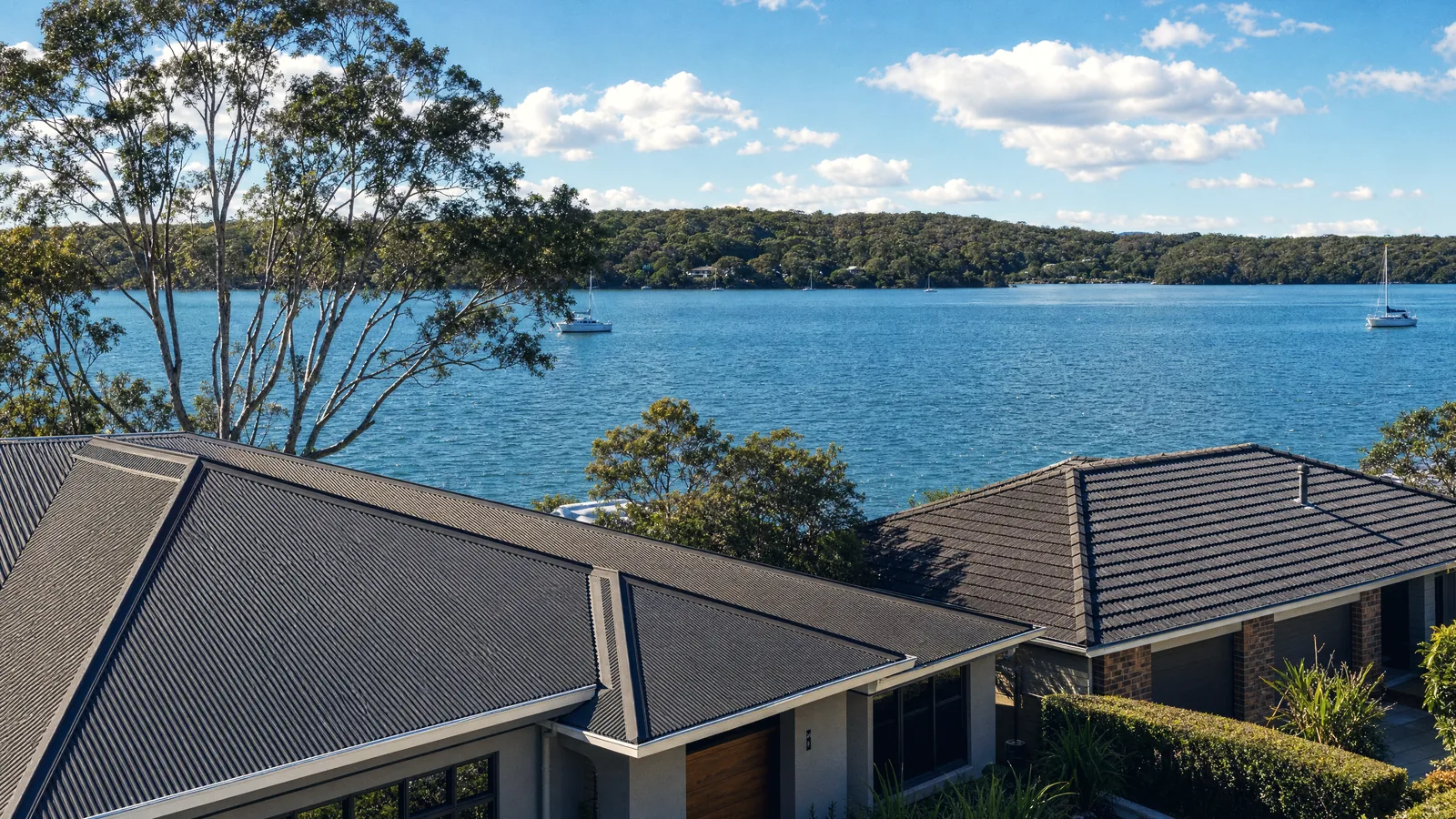 Tile and Colorbond rooftops stepping down toward Lake Macquarie, with the water behind them