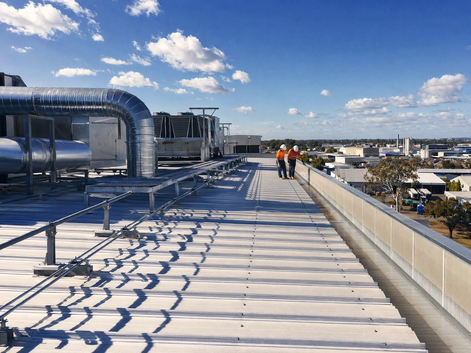 Large industrial metal roof with services and ductwork running across it, box gutter visible along the parapet